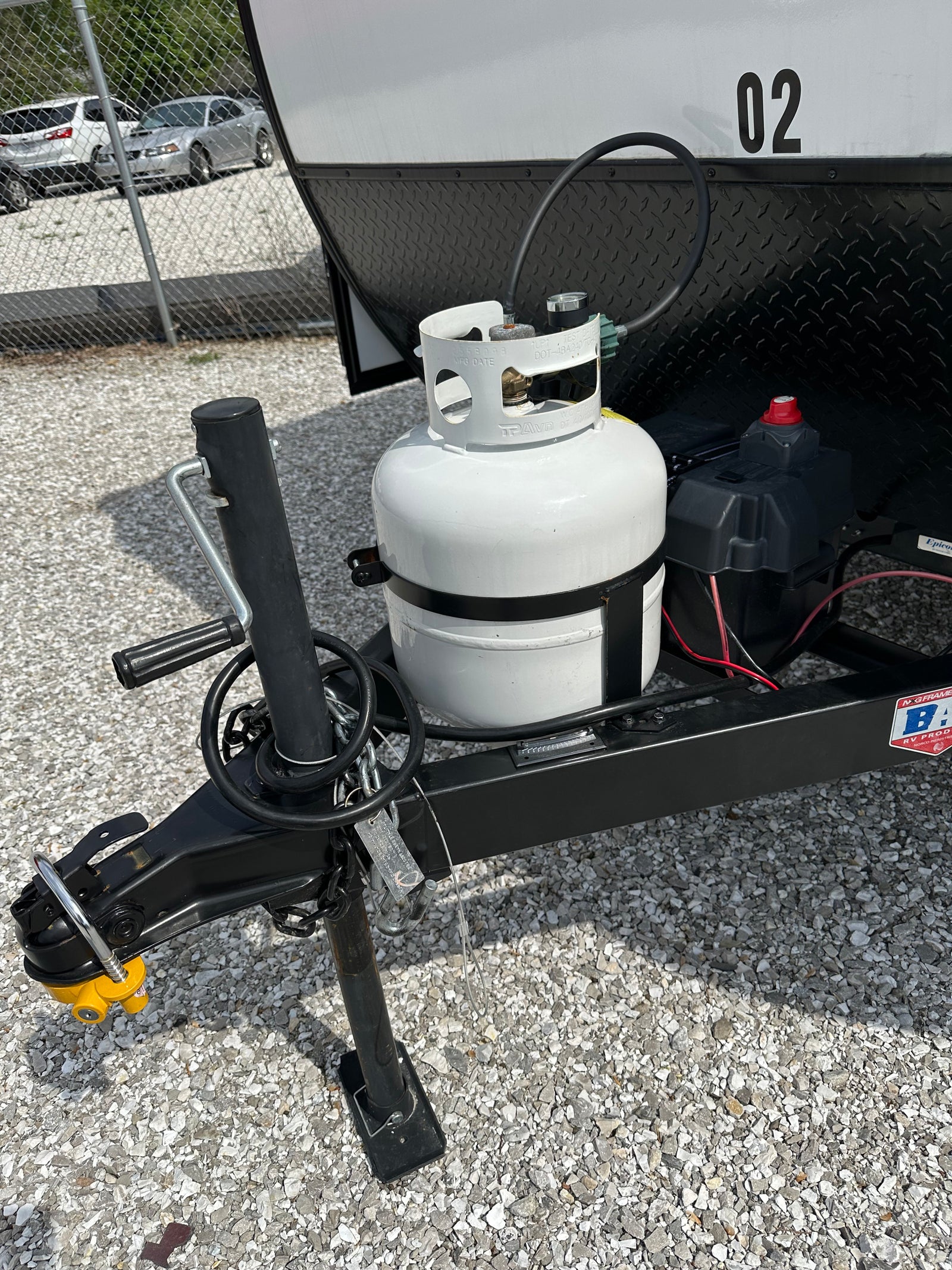 RV rental trailer's front end, showcasing the hitch, propane tank, and battery setup for road travel.