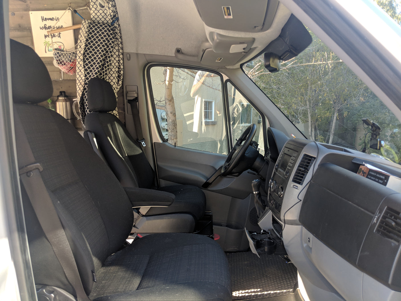 RV rental interior: Front cabin with black seats, steering wheel, dashboard, and a "Home is where we park it" sign.