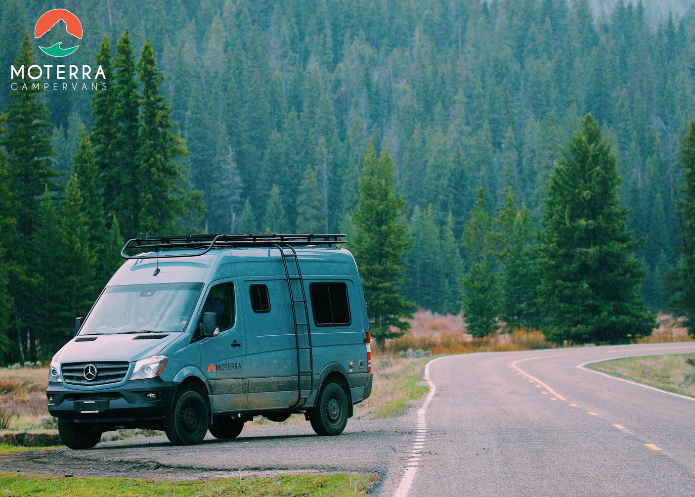 Blue Moterra camper van parked on a winding road amidst a dense forest, ideal for your next rv rental adventure.