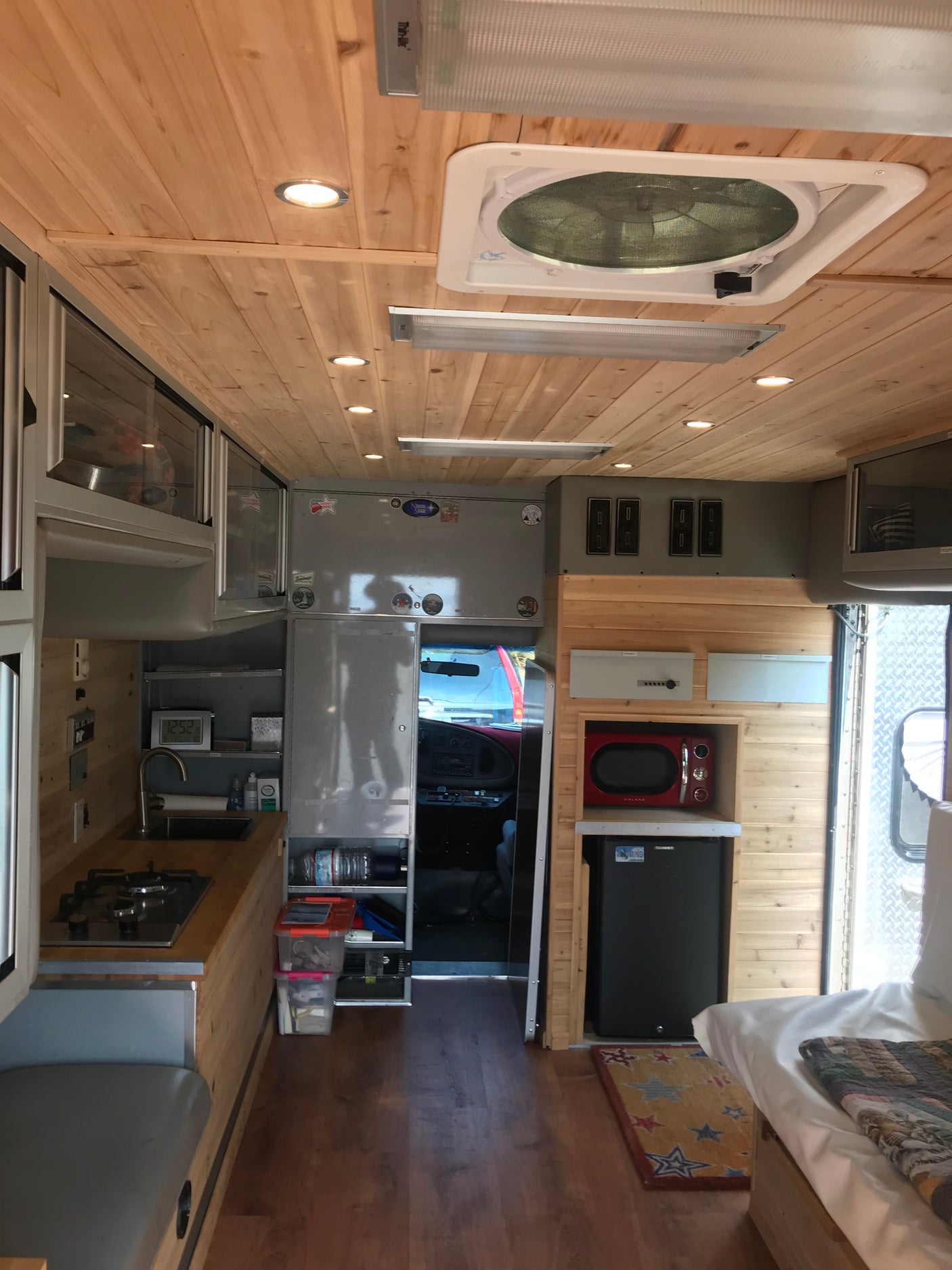 RV rental camper interior: cozy mobile kitchen, bed, fridge, microwave, and wood-paneled ceiling.