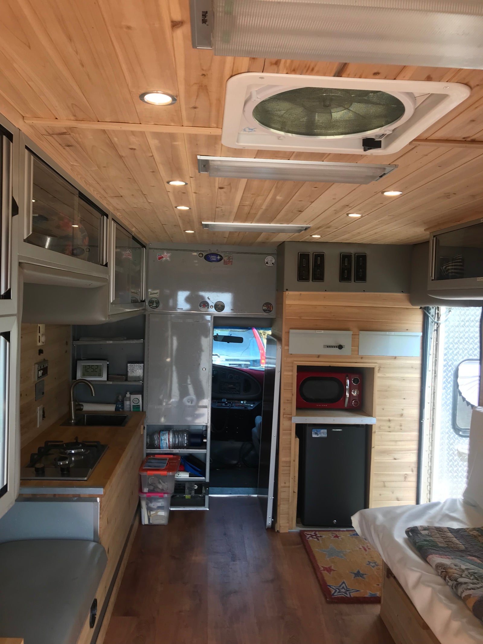 RV rental camper interior: cozy mobile kitchen, bed, fridge, microwave, and wood-paneled ceiling.