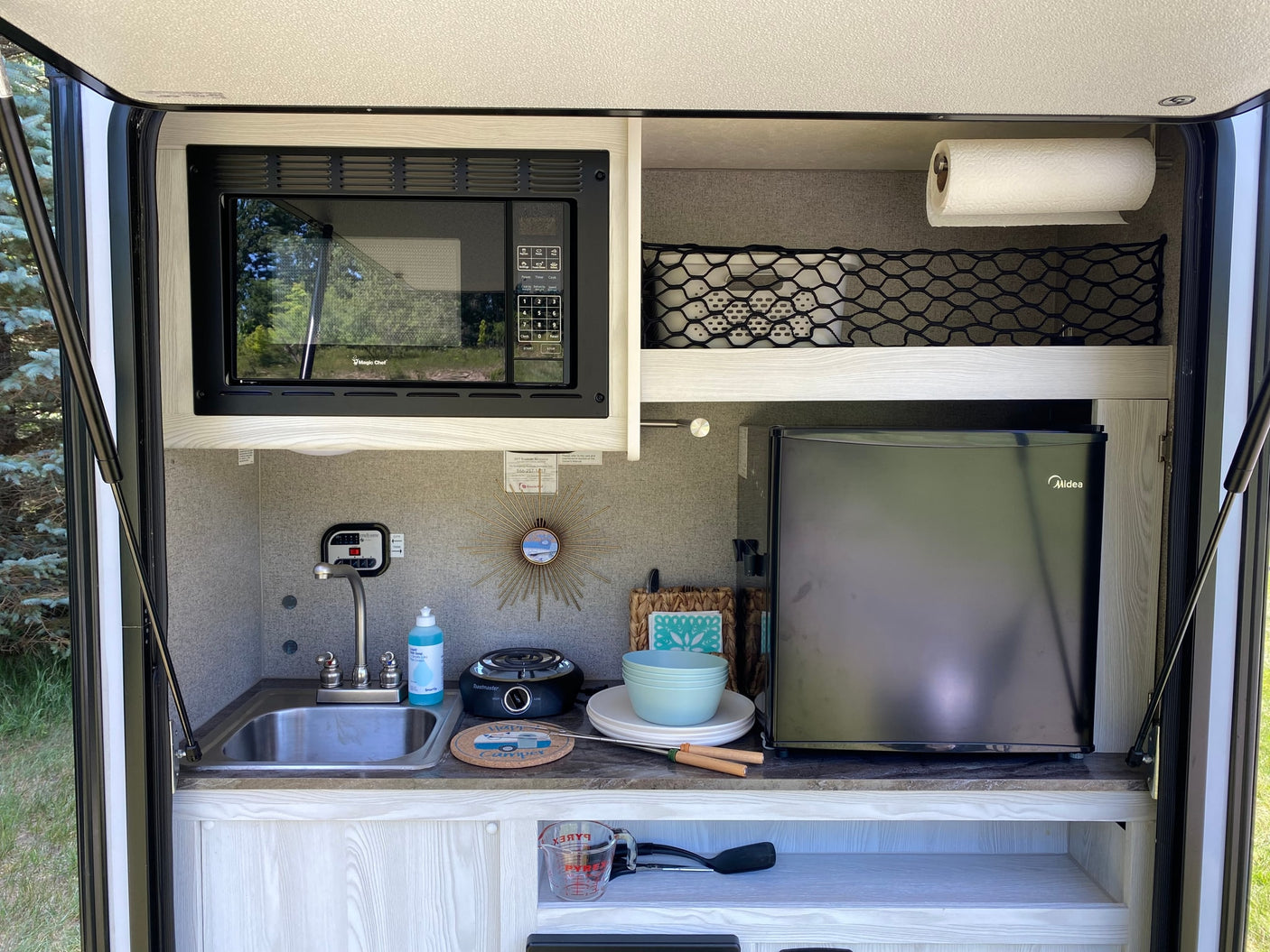 This rv rental outdoor kitchen has a Magic Chef microwave, sink, Midea fridge, and Toastmaster hot plate, ready for camping.
