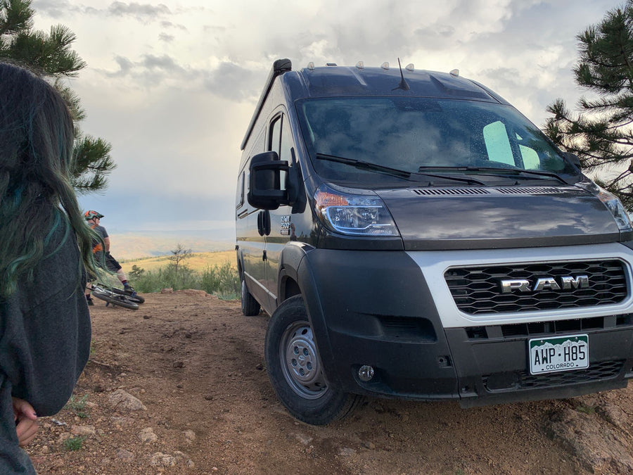 Off-road RV rental adventure! A dark Ram camper van & mountain bikers on a scenic Colorado dirt trail.