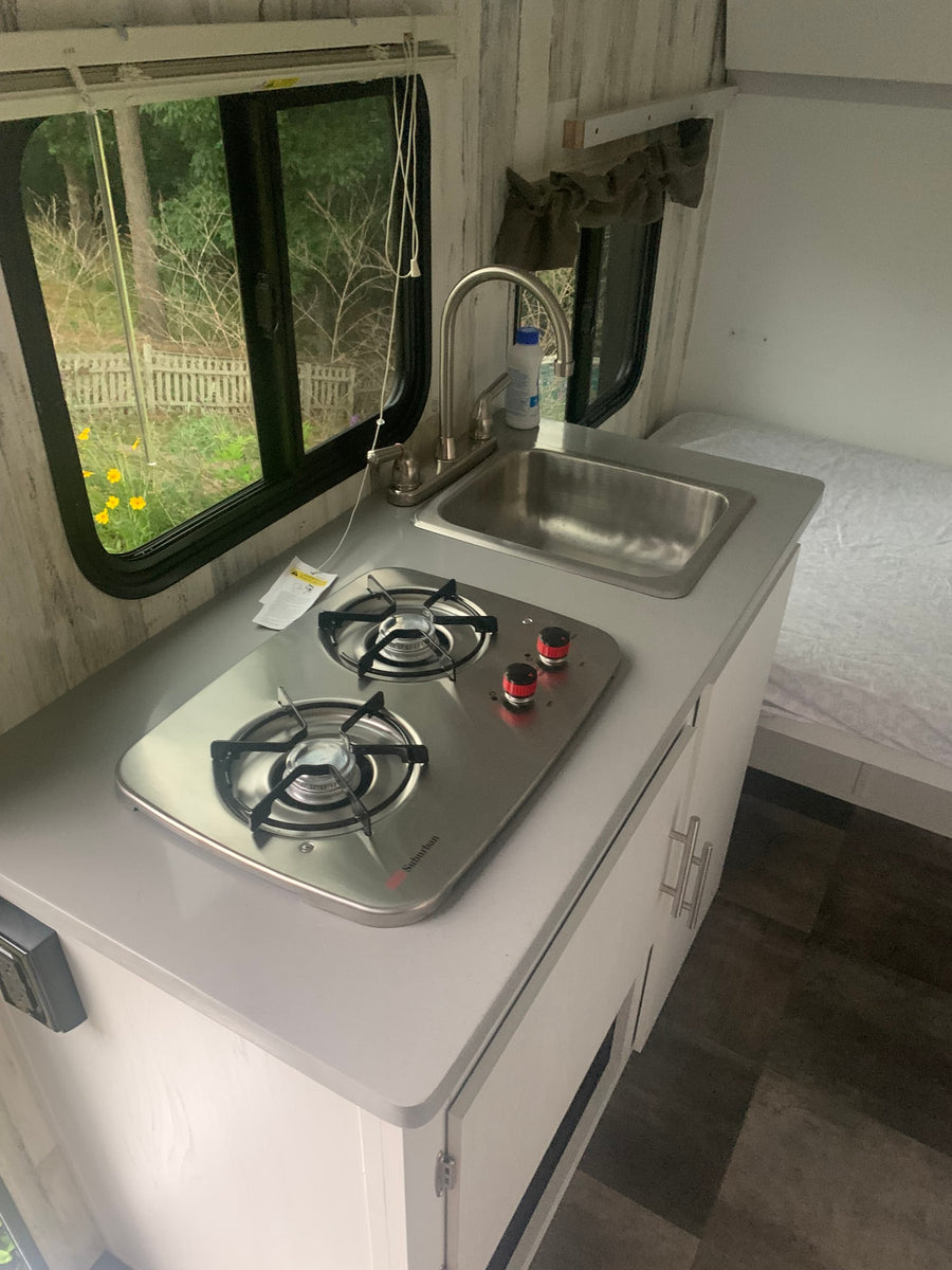 Bright RV rental interior featuring a compact kitchen with a sink, Suburban stove, and cozy sleeping area.