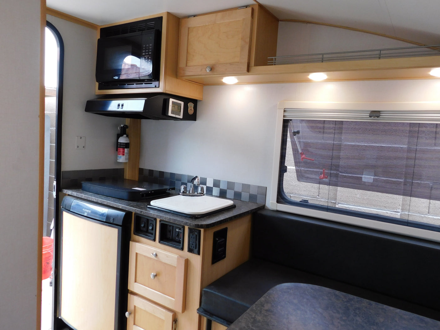 RV rental kitchen: microwave, sink, fridge, fire extinguisher, and cozy dinette for travel.