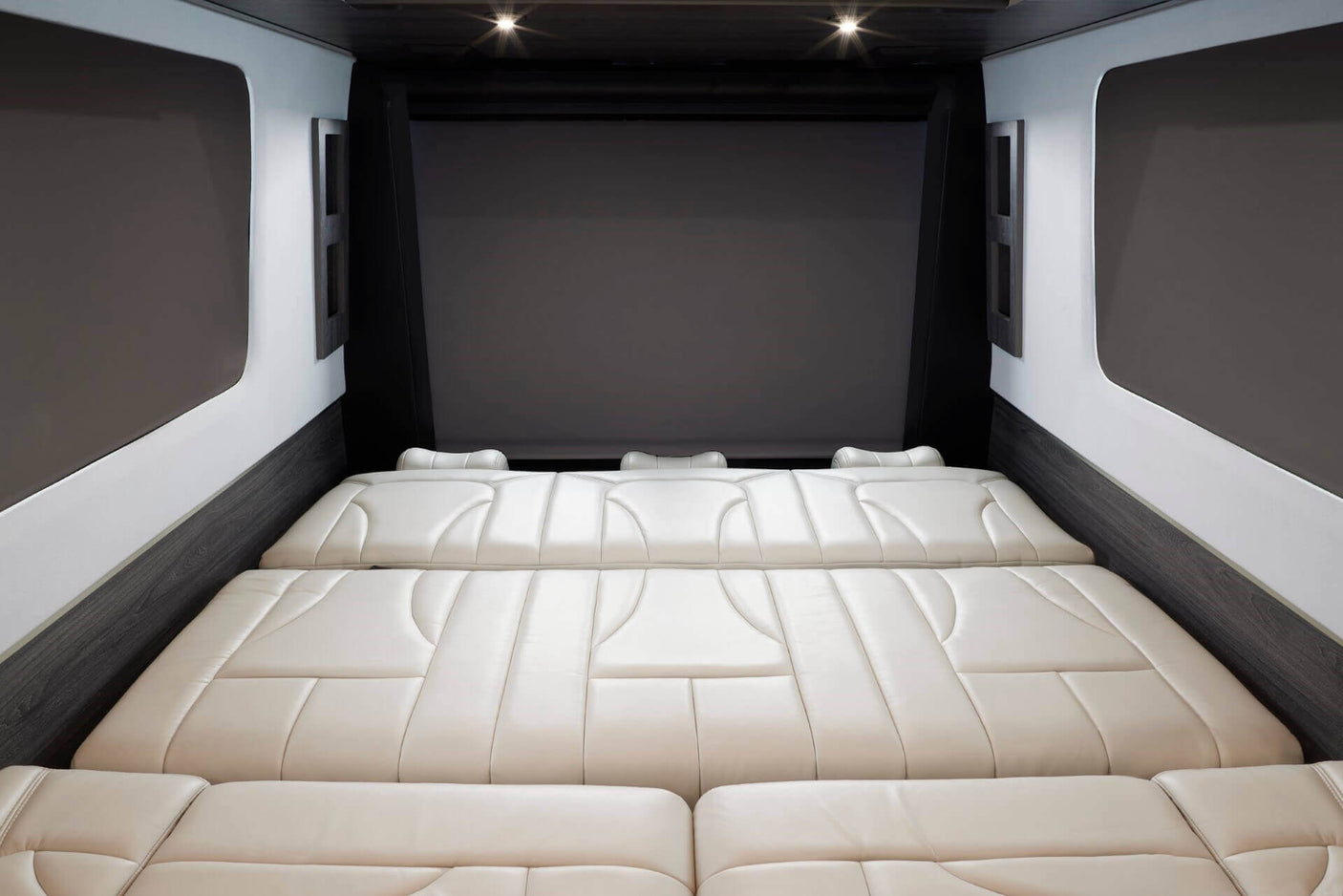 Luxury RV rental interior featuring a spacious, cream-colored modular bed/seating area, with a large screen overhead.