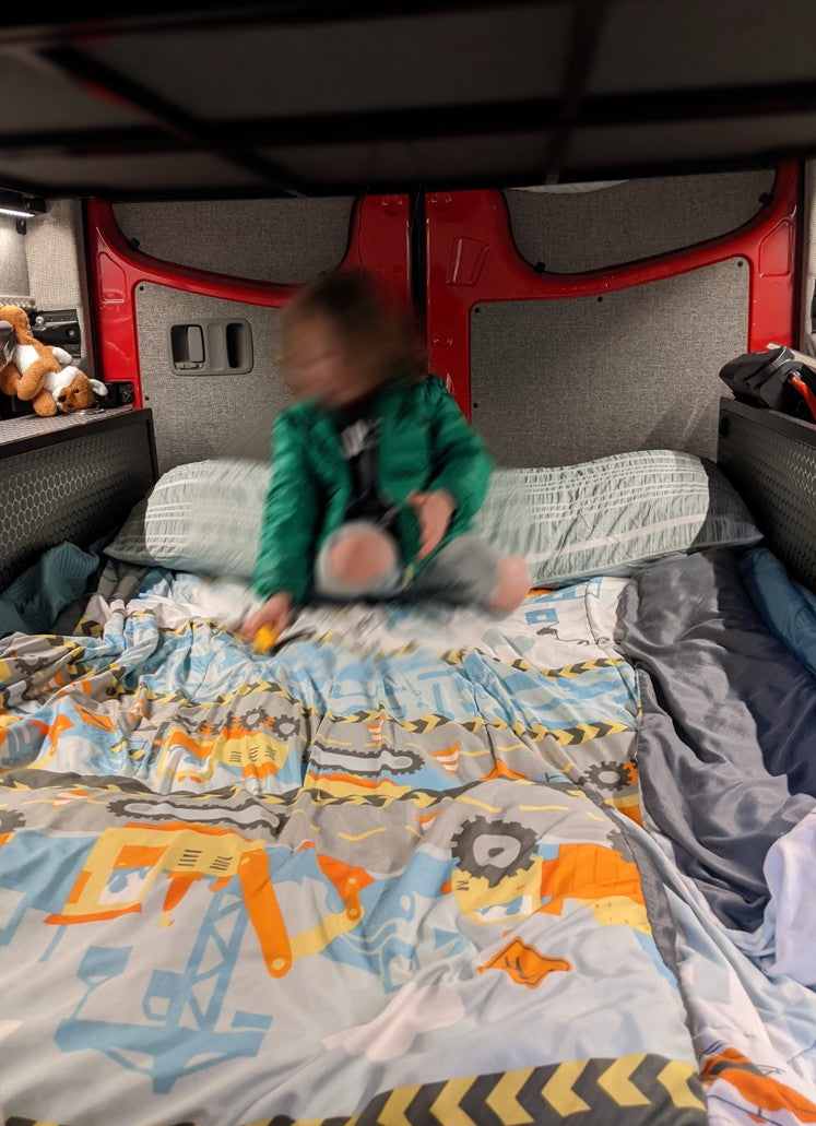 and a fire extinguisher.|Cozy RV rental camper van interior. A bed with a green pillow and striped comforter offers a serene view of autumn trees.|Explore this RV rental's cozy interior: a converted camper van kitchen with a colorful tiled backsplash
