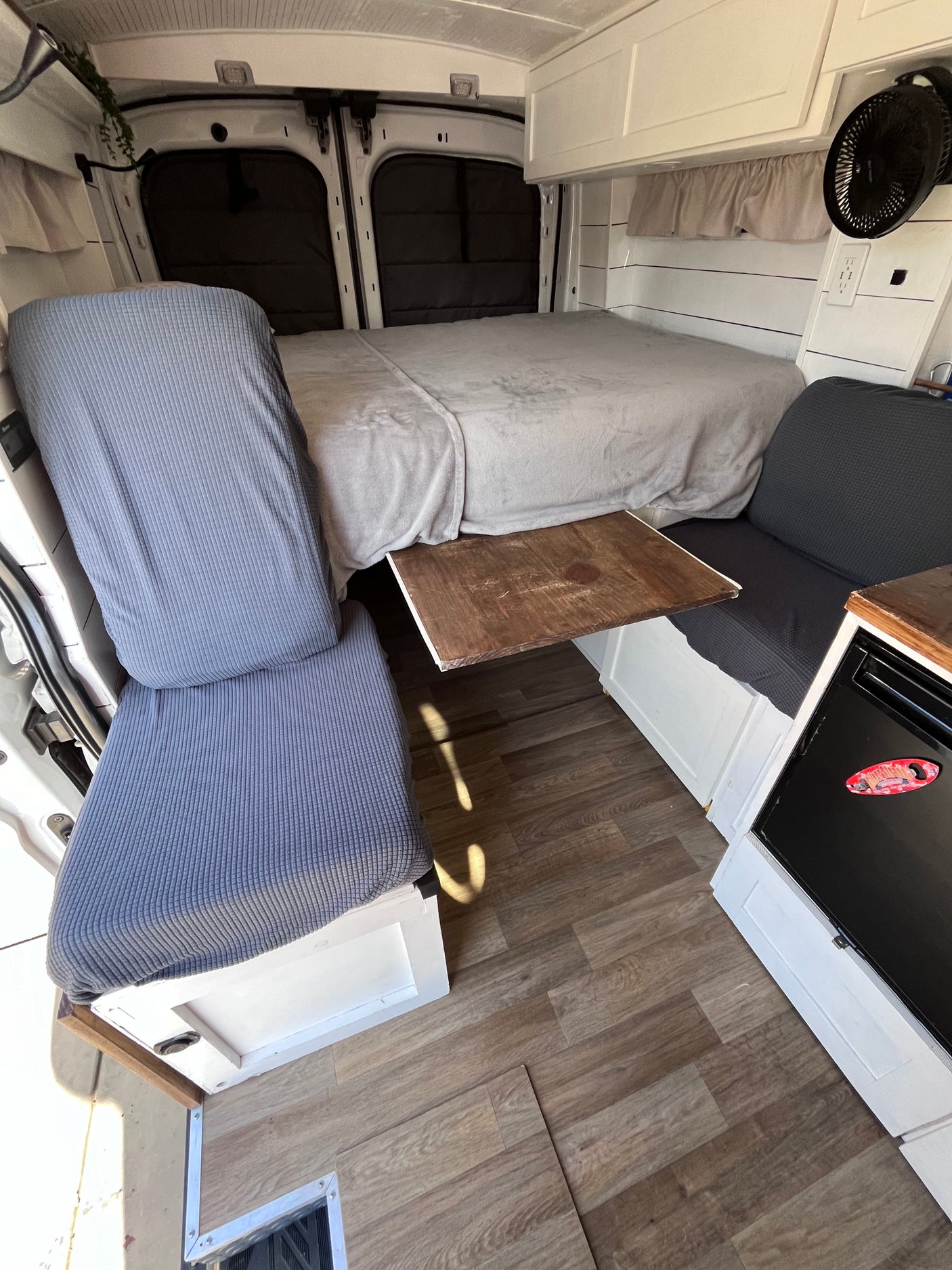 Cozy RV rental interior with a comfy bed, bench seating, and a rustic wood table. Enjoy mobile living in this van.