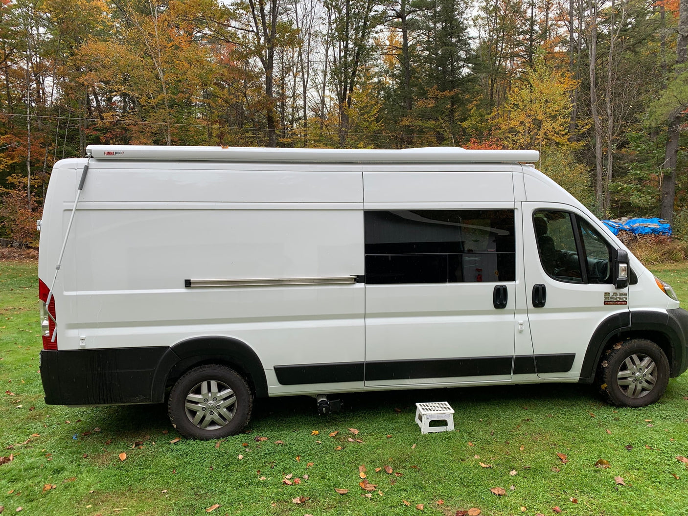 White Ram ProMaster camper van, ideal for rv rental adventures, parked on grass amidst autumn trees.