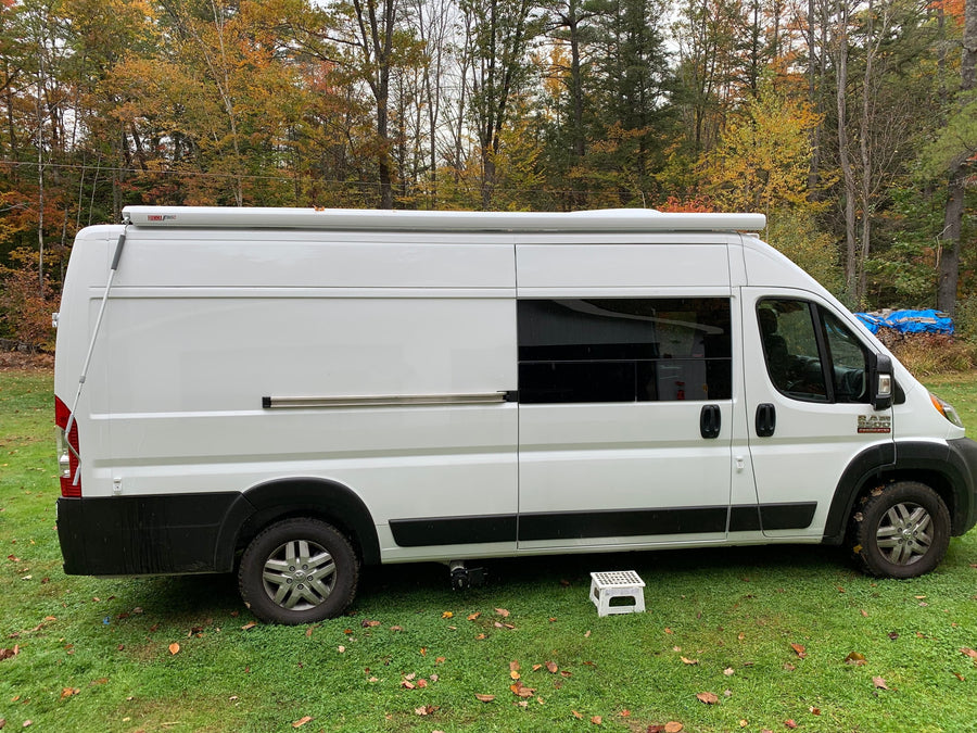 White Ram ProMaster camper van, ideal for rv rental adventures, parked on grass amidst autumn trees.