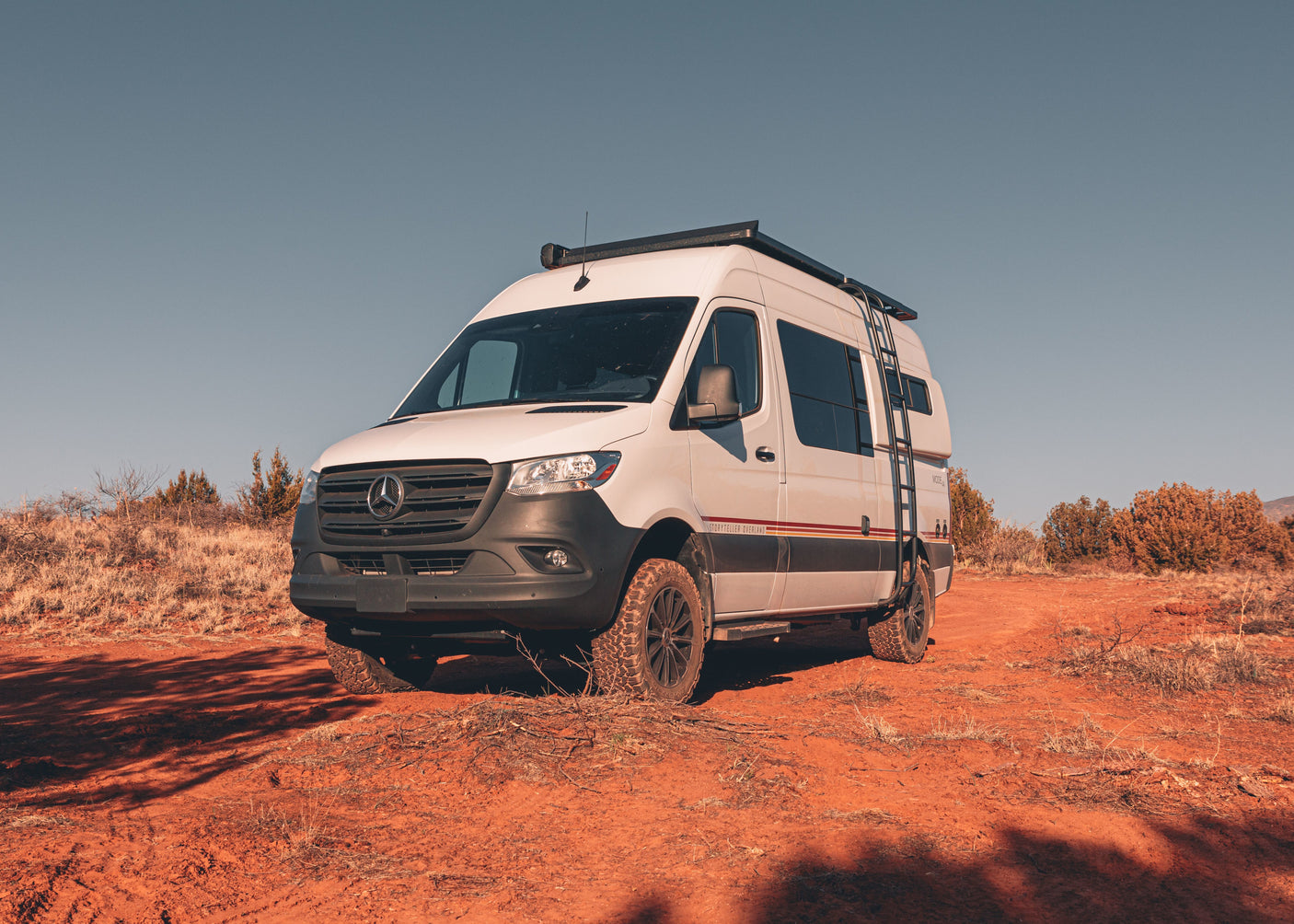 This Storyteller Overland Mercedes Sprinter **rv rental** camper van is ready for off-road adventure on red desert terrain.