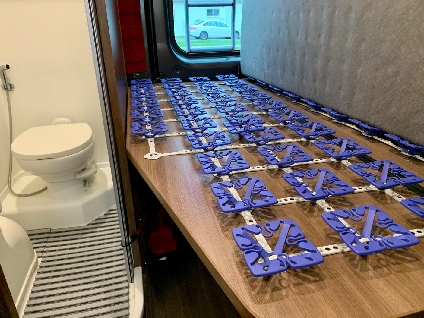 RV rental interior: compact bathroom with toilet and a bed base featuring purple mattress suspension modules.
