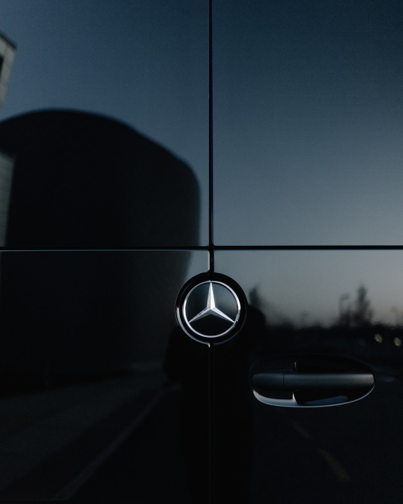 A dark Mercedes-Benz rv rental's side, showing its iconic star logo and door handle. Reflections add detail to the sleek panel.