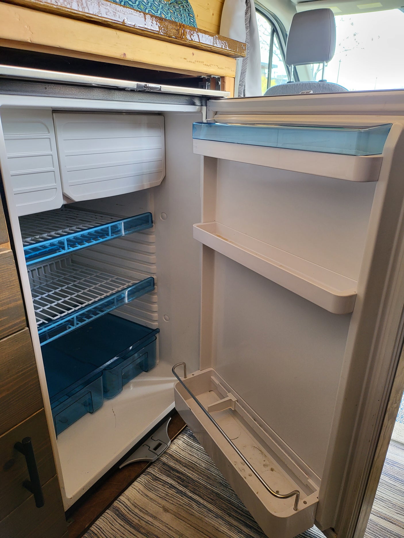 An open RV rental refrigerator and freezer, showing interior shelves and storage bins ready for your trip.
