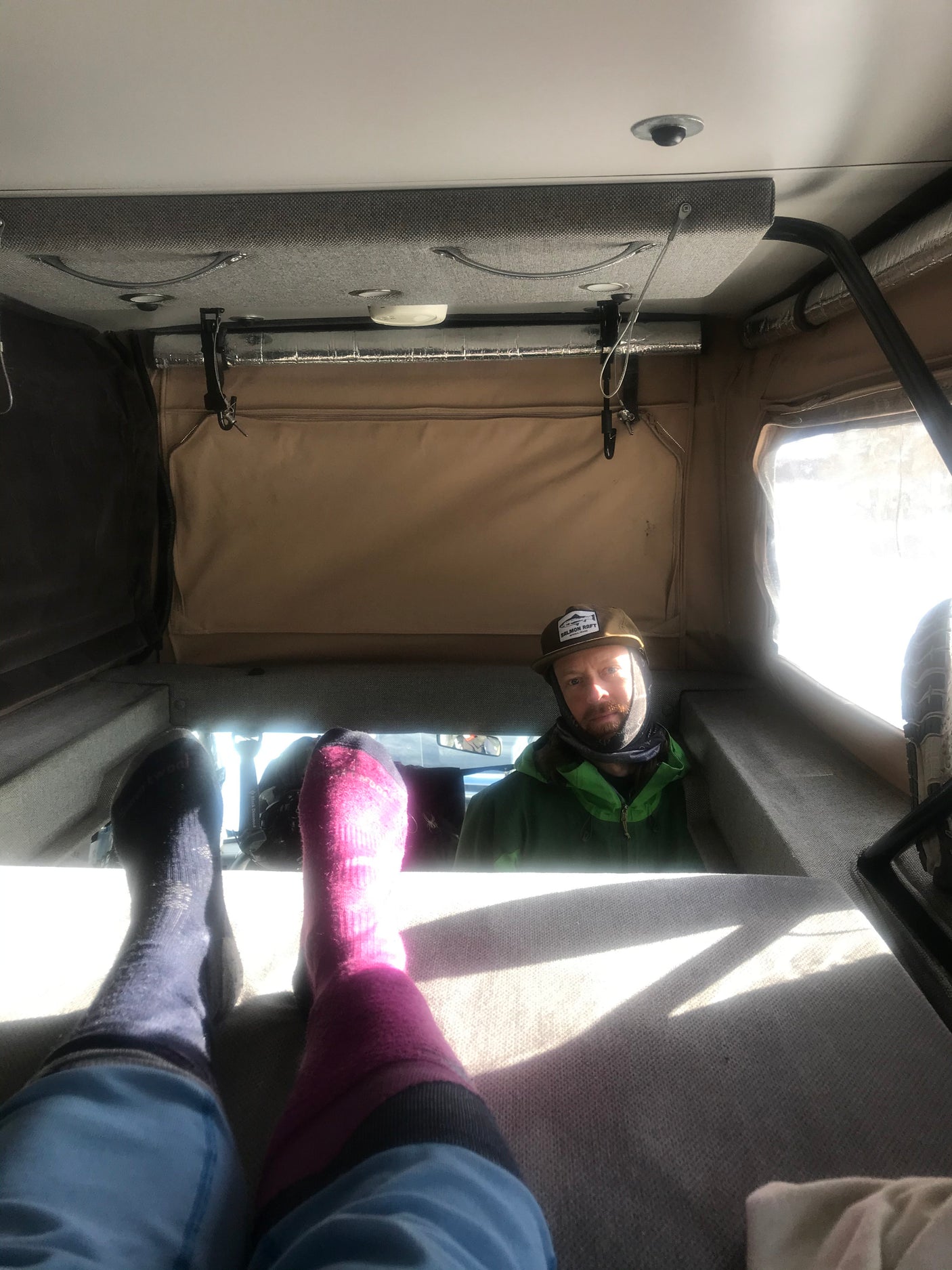 Feet up, relaxing inside a cozy rv rental, looking at a man in a hat and green jacket.