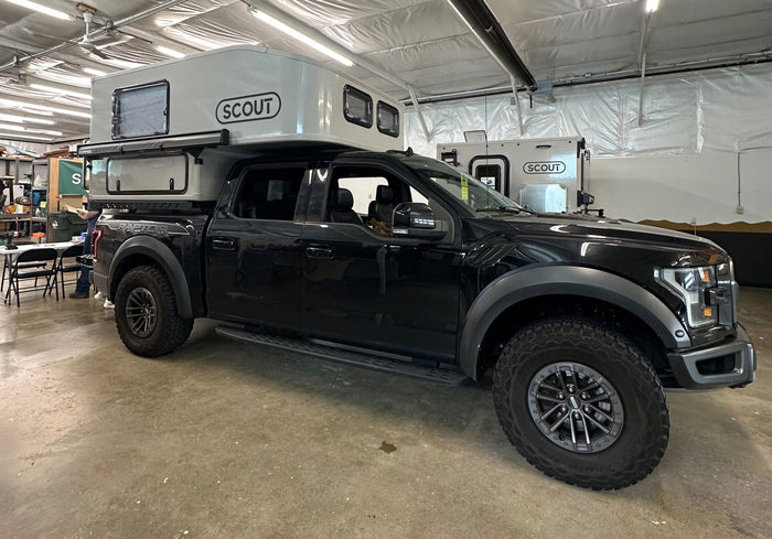 A black Ford Raptor pickup truck equipped with a light grey Scout truck camper, a popular type of RV for rental.