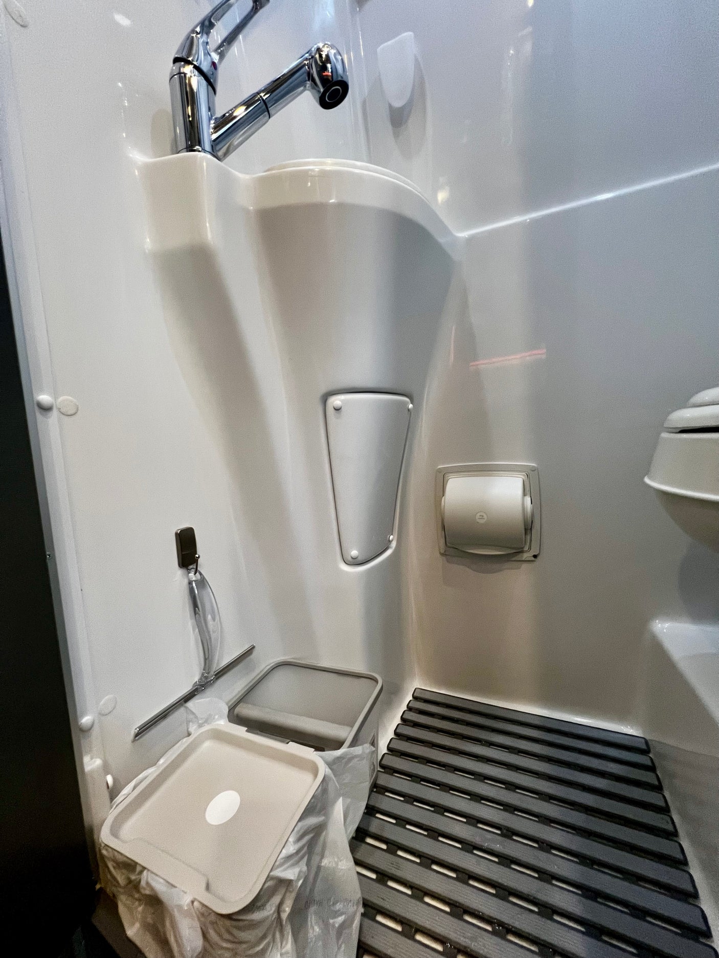 RV rental's compact wet bath: sink, faucet, toilet, toilet paper holder, and slatted floor mat. Designed for efficiency.