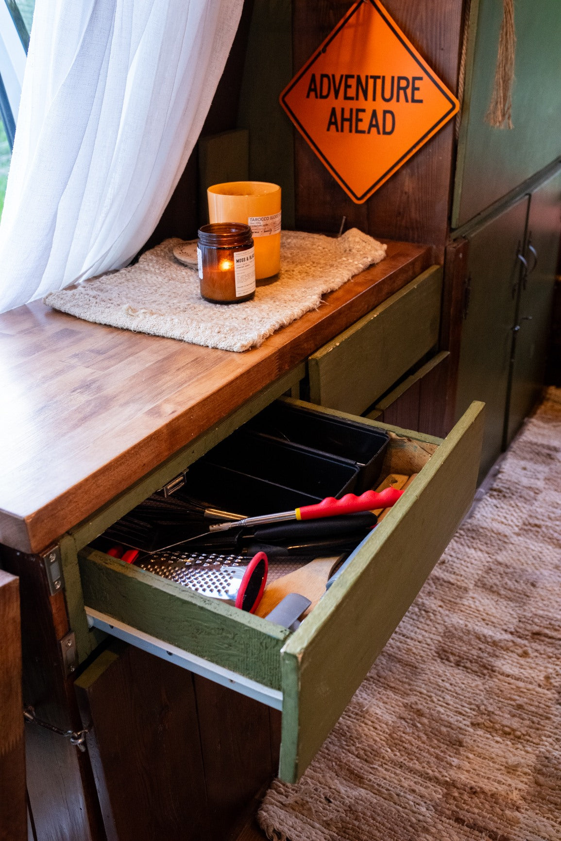 Stay organized in this RV rental's kitchen: an open drawer reveals cooking utensils beside a cozy counter with a lit candle.