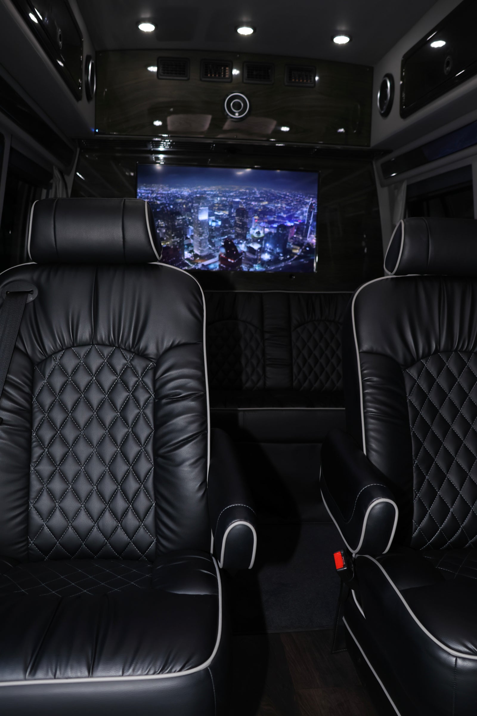 Luxury RV rental interior featuring black quilted leather seats with white piping and a large screen displaying a city night view.