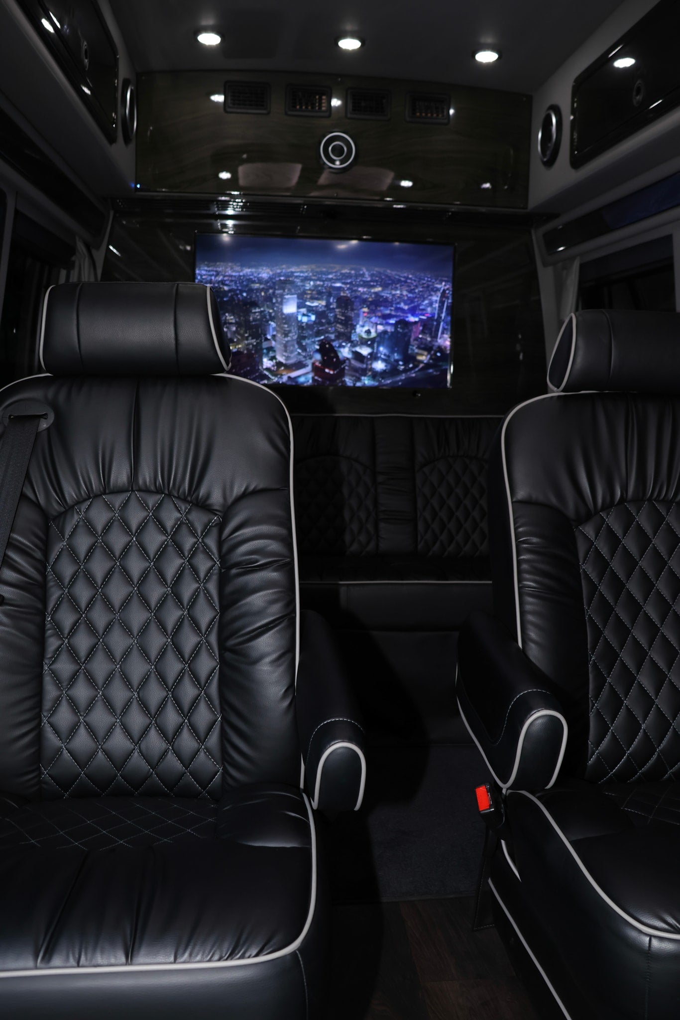 Luxury RV rental interior featuring black quilted leather seats with white piping and a large screen displaying a city night view.