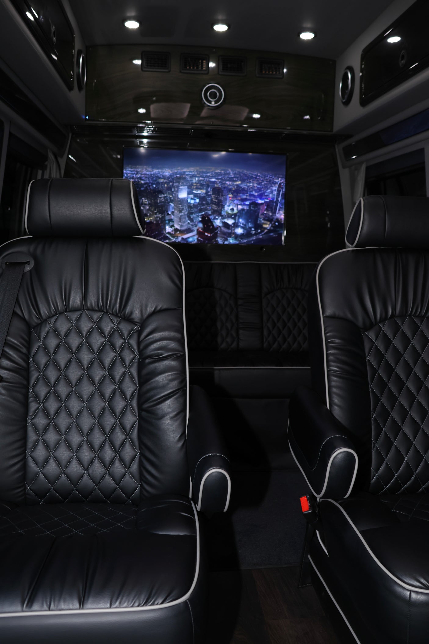 Luxury RV rental interior featuring black quilted leather seats with white piping and a large screen displaying a city night view.