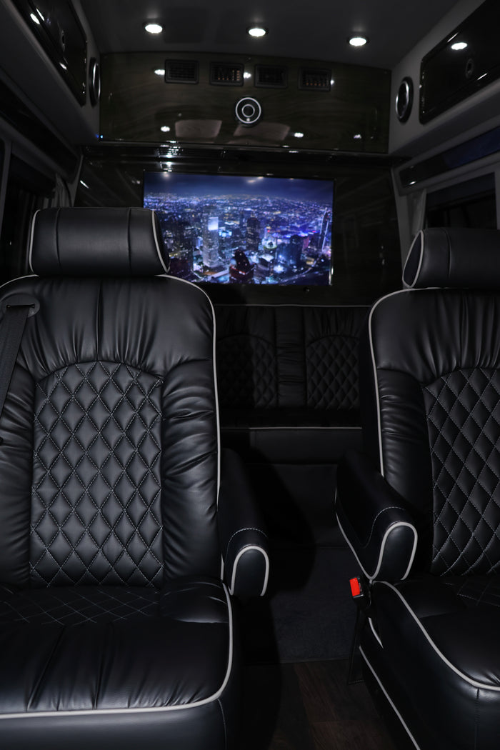 Luxury RV rental interior featuring black quilted leather seats with white piping and a large screen displaying a city night view.