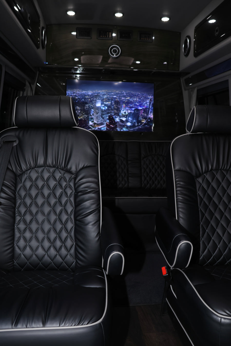 Luxury RV rental interior featuring black quilted leather seats with white piping and a large screen displaying a city night view.