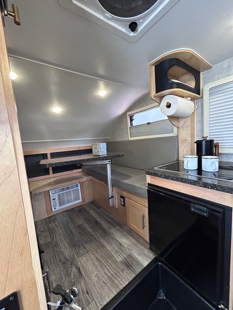 RV rental interior features a compact dinette, kitchenette with sink & fridge, plus AC. Ideal for cozy adventures.