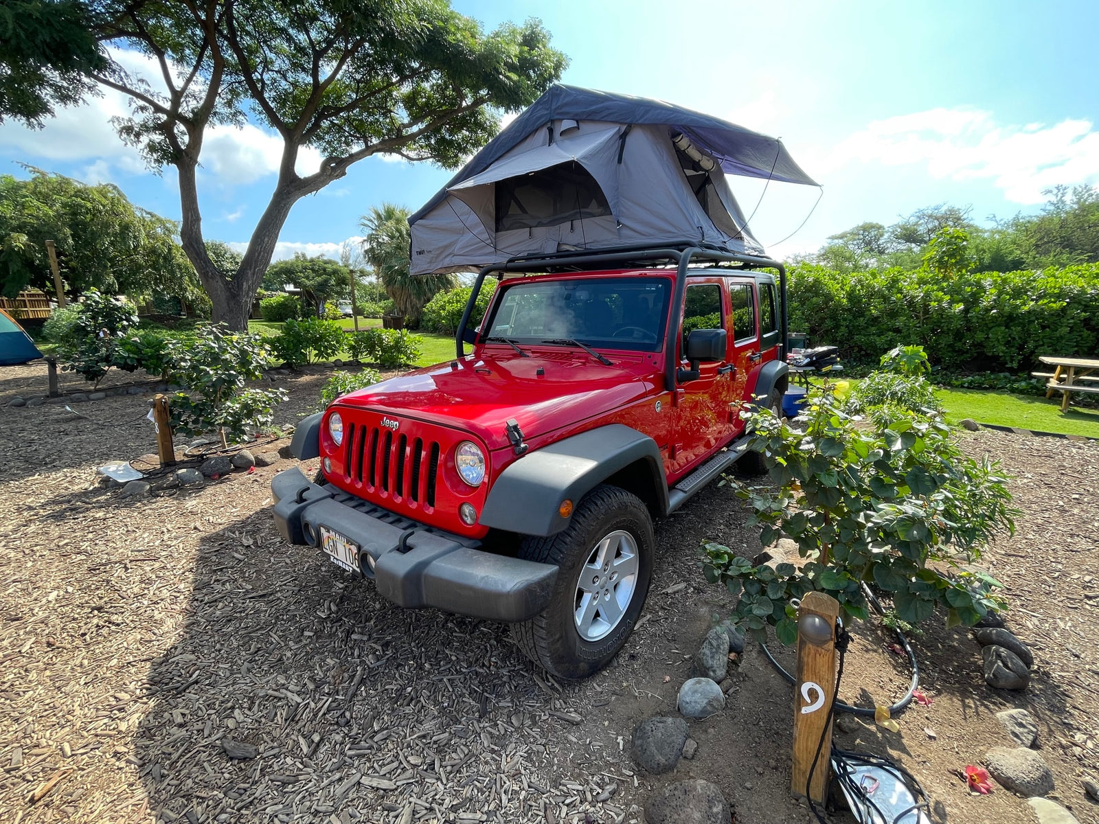 Red Jeep with rooftop tent deployed at a sunny outdoor campsite, ideal for your next RV rental adventure.