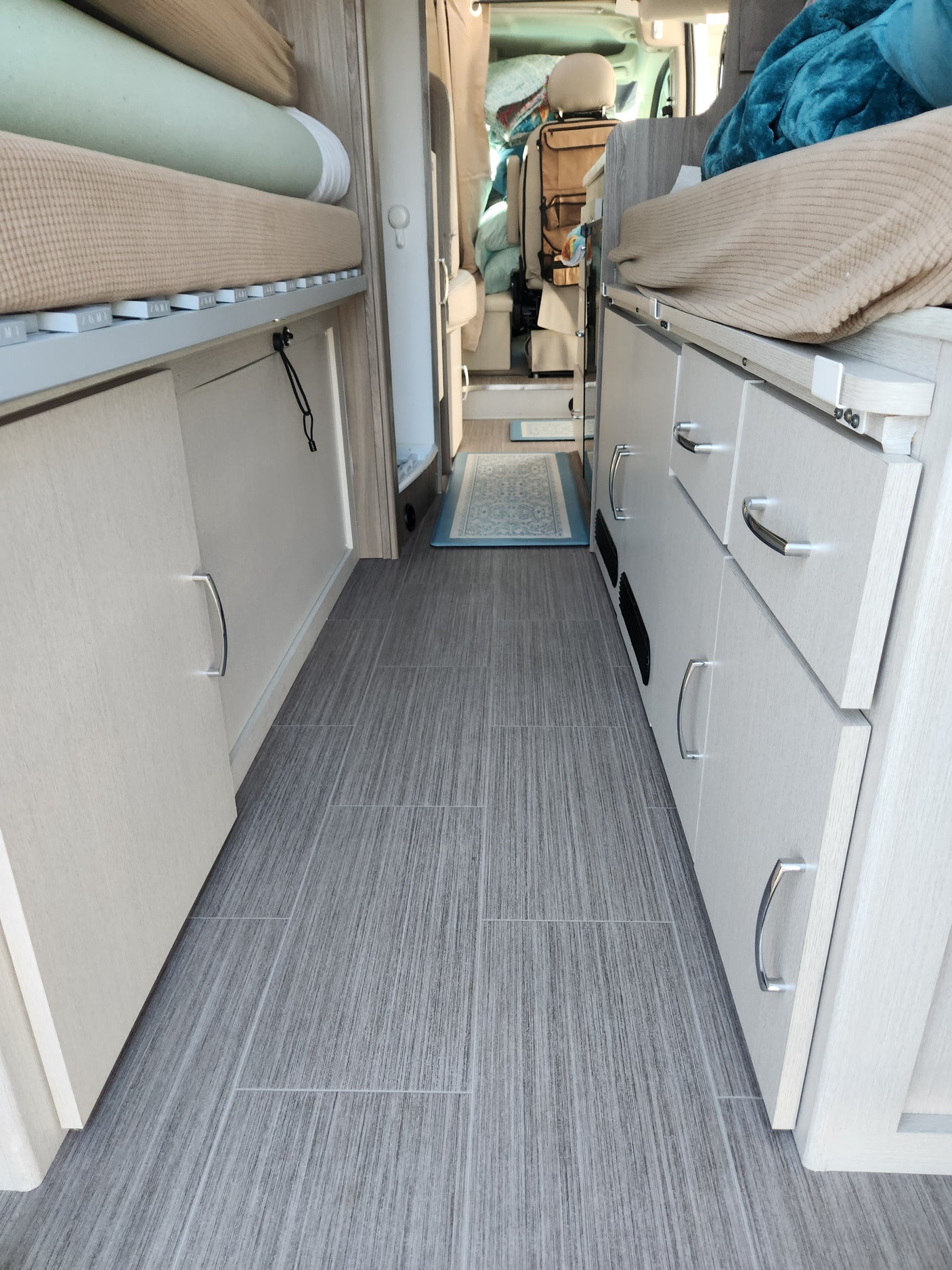 This RV rental interior features modern light wood cabinets, an organized sleeping area, and sleek gray wall panels.