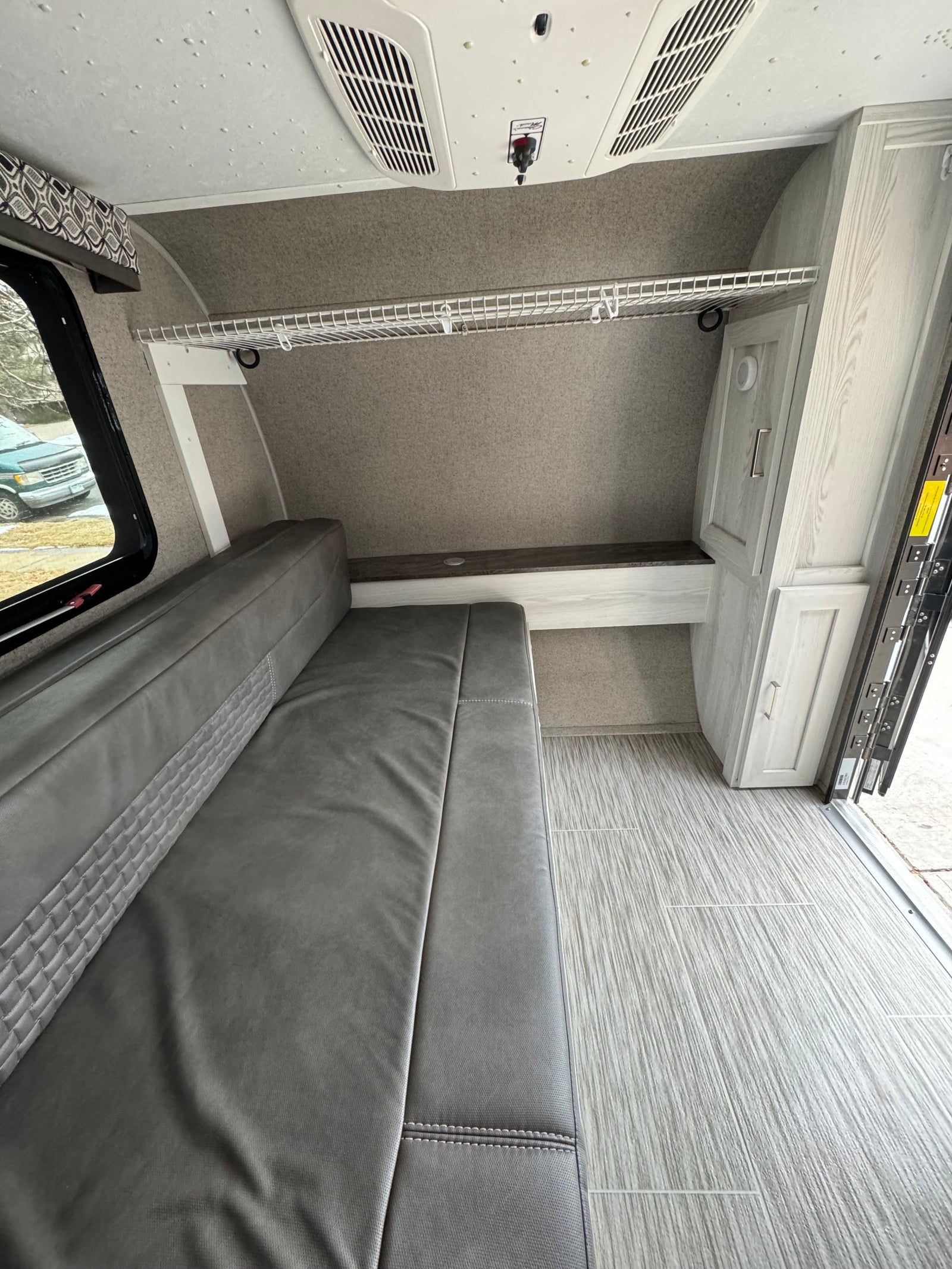 RV rental interior shows grey dinette/bed, ceiling AC, wire shelf, and light wood-look flooring.