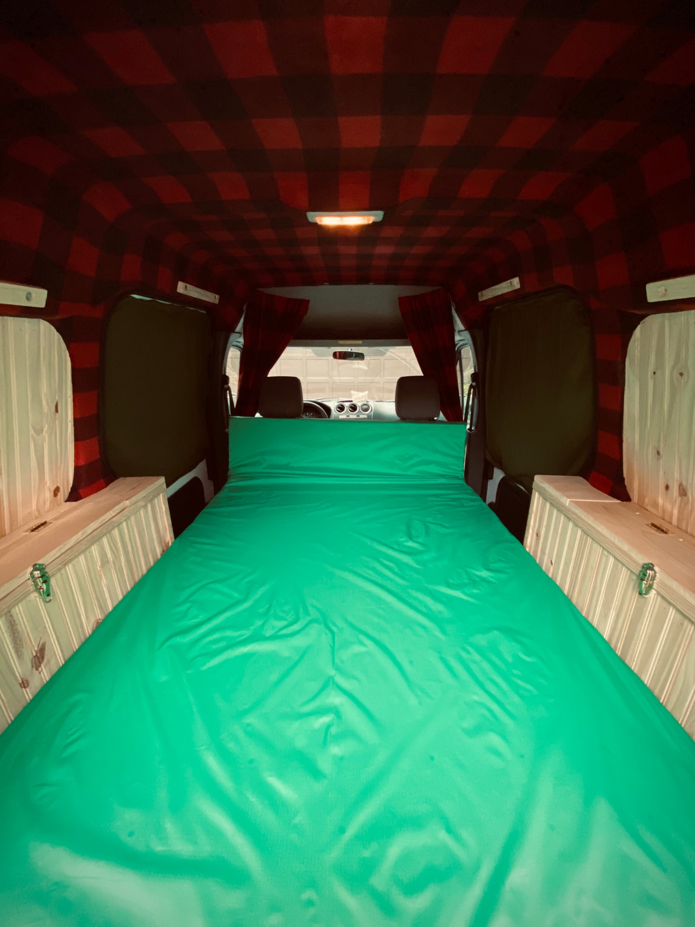 Cozy camper van interior: vibrant green bed, plaid ceiling, and wooden storage for a comfortable RV rental experience.