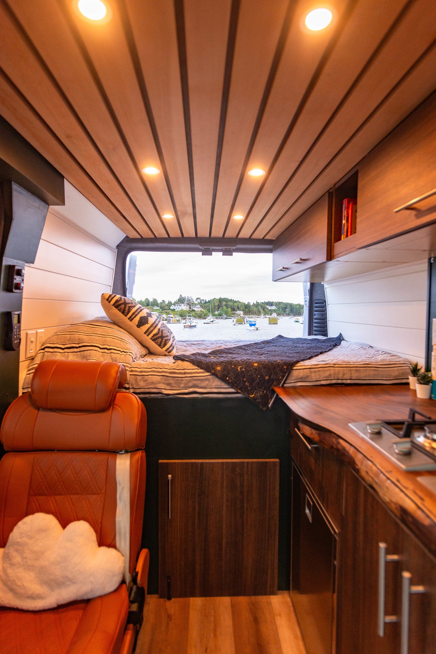 Inside this custom RV rental: wood-paneled ceiling, comfy bed, and a kitchen area, all with an ocean view.