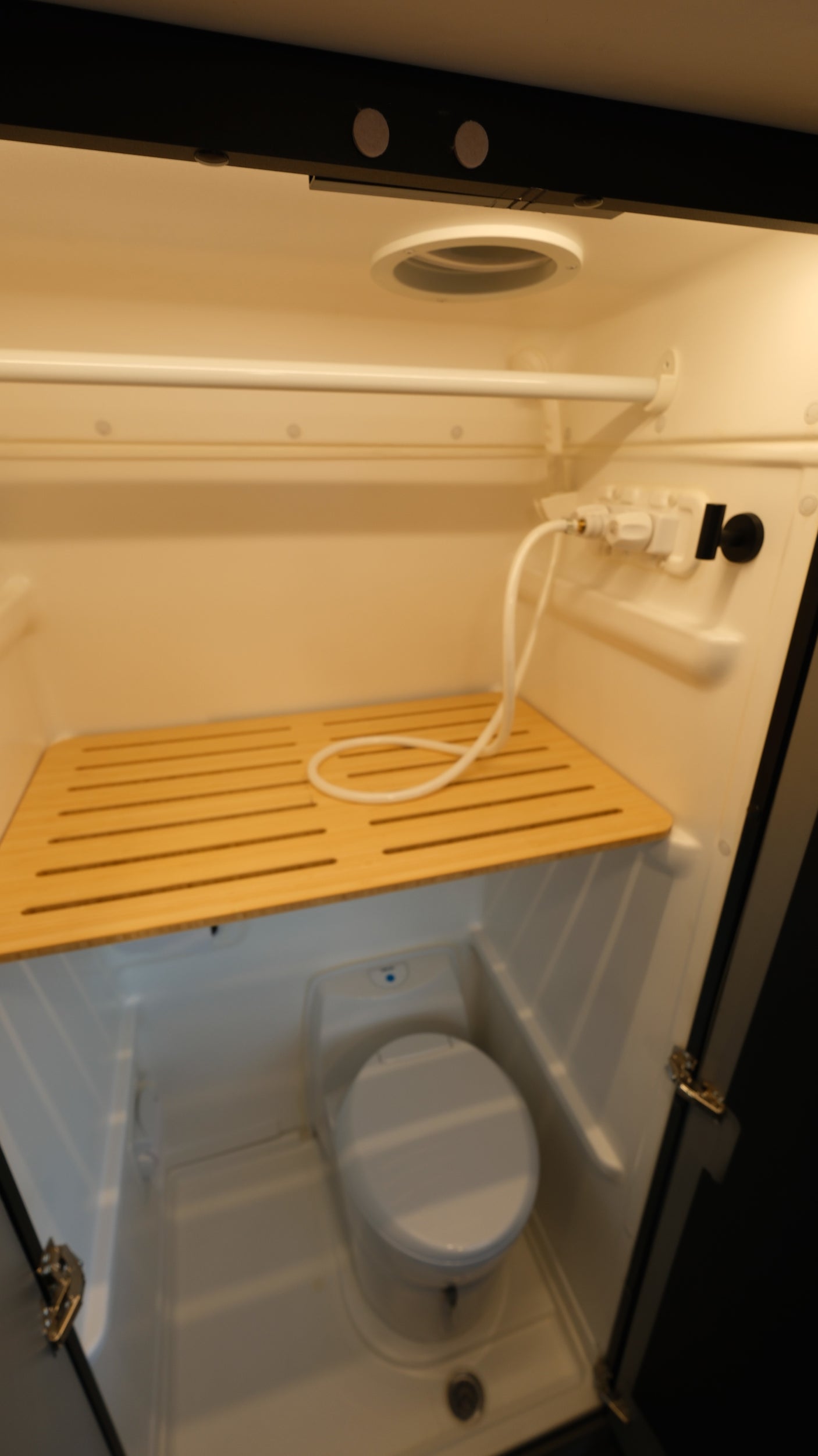 Compact RV rental bathroom with shower, toilet, and wooden mat, ideal for road trips.