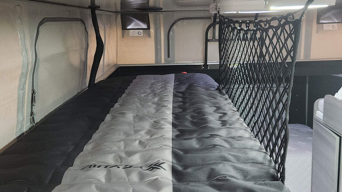 Explore an RV rental's sleeping area: a compact bunk bed with a two-tone gray mattress and safety net for secure, comfortable travel.