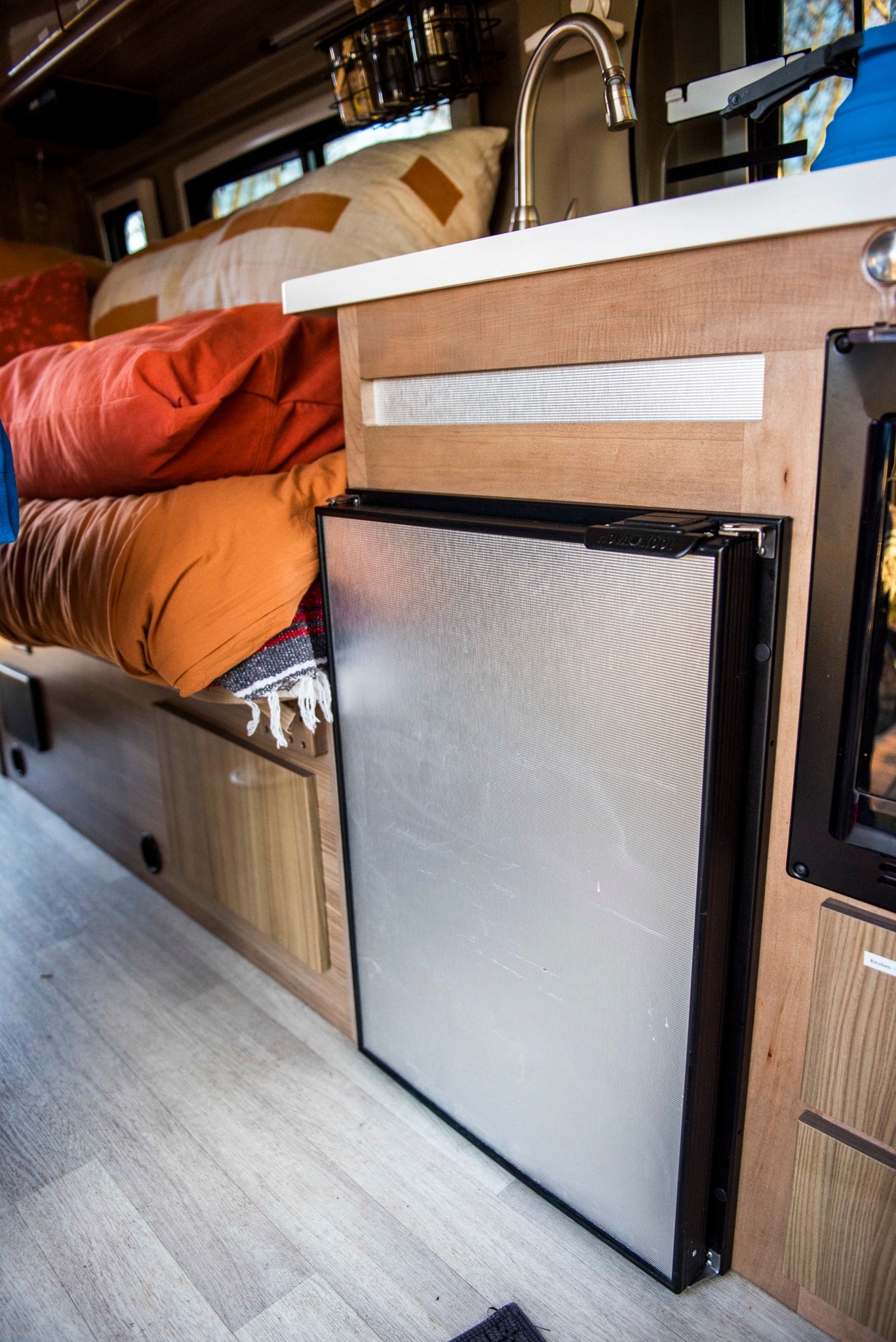 Compact RV rental interior showcasing a modern fridge, sink, and a comfortable bed for road trips.