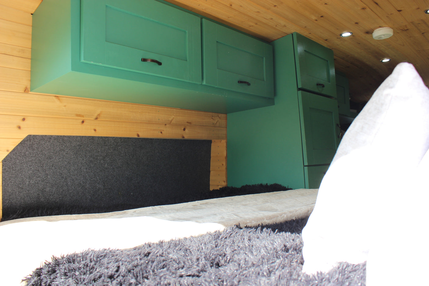 Cozy RV rental interior with green cabinets, wooden walls/ceiling, and a comfy bed setup.