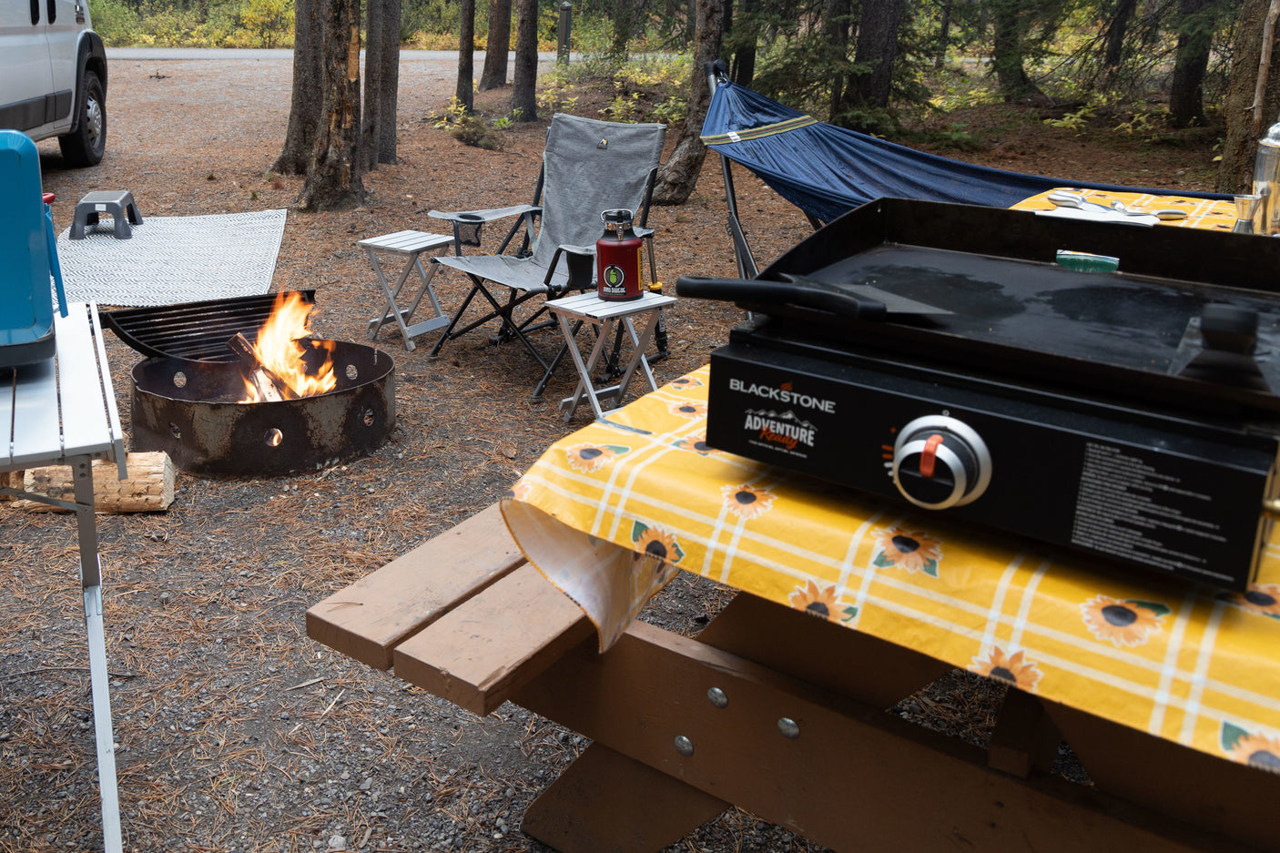 RV rental camping setup with a Blackstone griddle, campfire, and hammock for a relaxing outdoor experience.