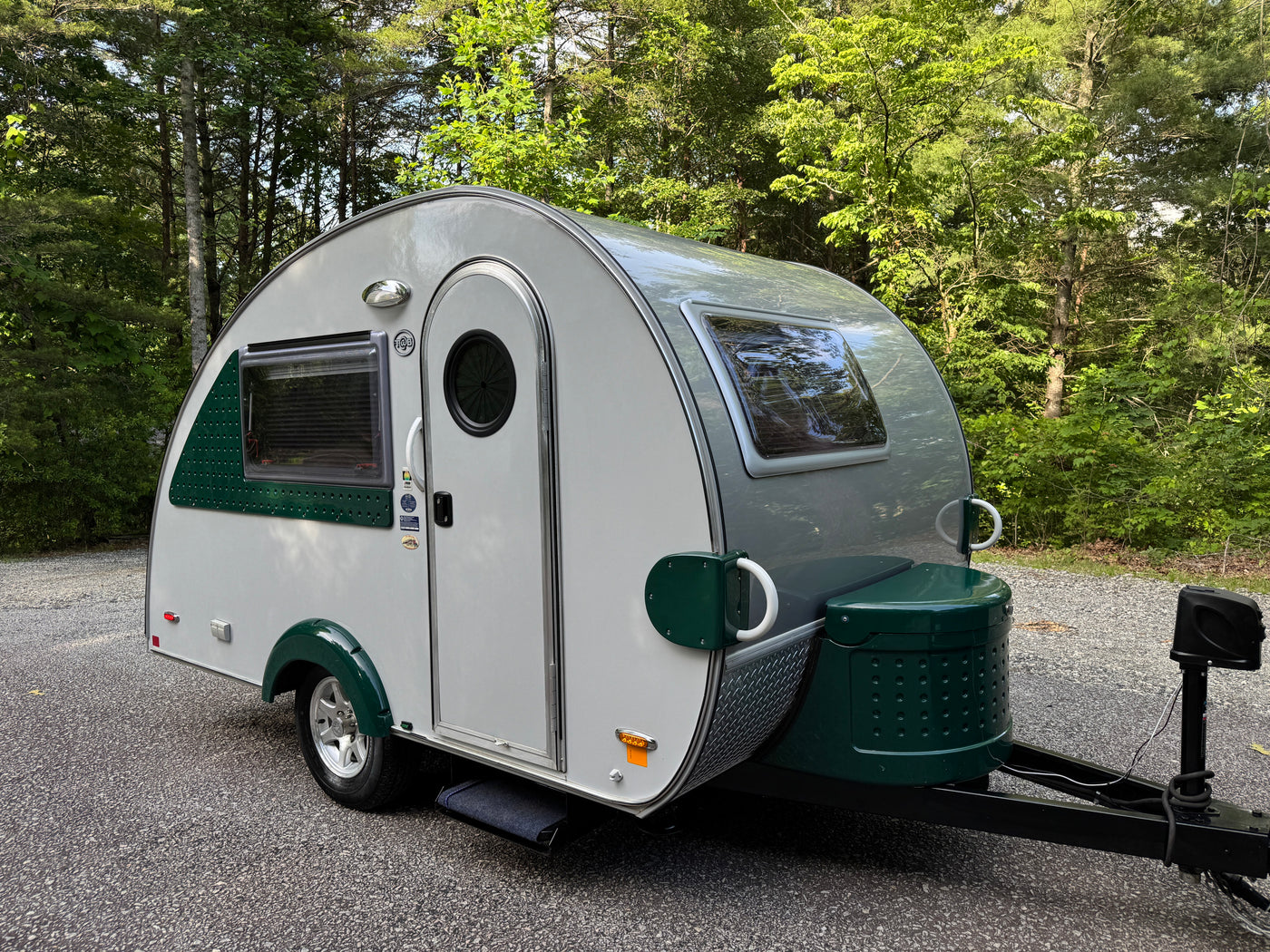 A compact, modern gray and green teardrop camper, great for an rv rental, is parked on gravel in a shaded forest setting. — photo 1