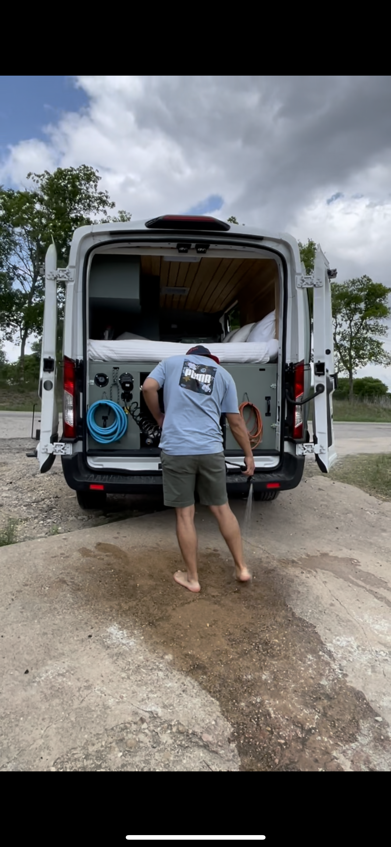 Barefoot man rinses off at the back of an RV rental. This custom camper van offers convenient outdoor water access.