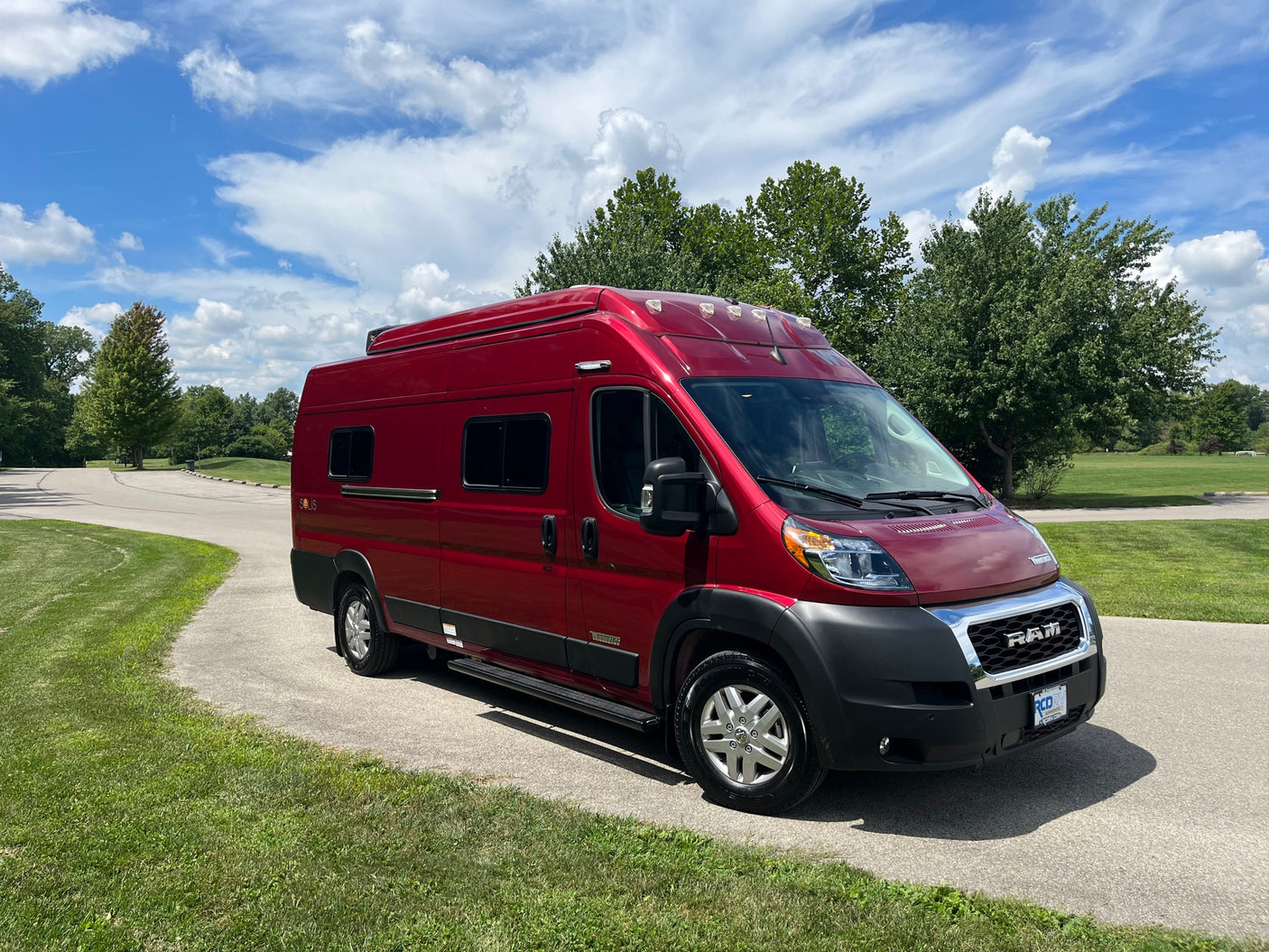 A vibrant red Winnebago Solis camper van, perfect for rv rental, parked on a paved path on a sunny day.