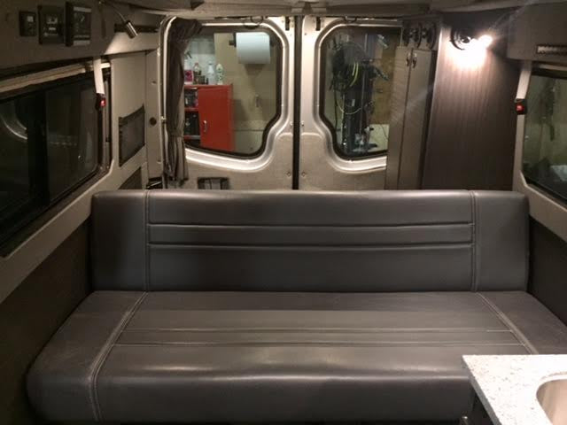 RV rental: View inside a camper van with a comfortable grey bench seat and rear cargo doors.