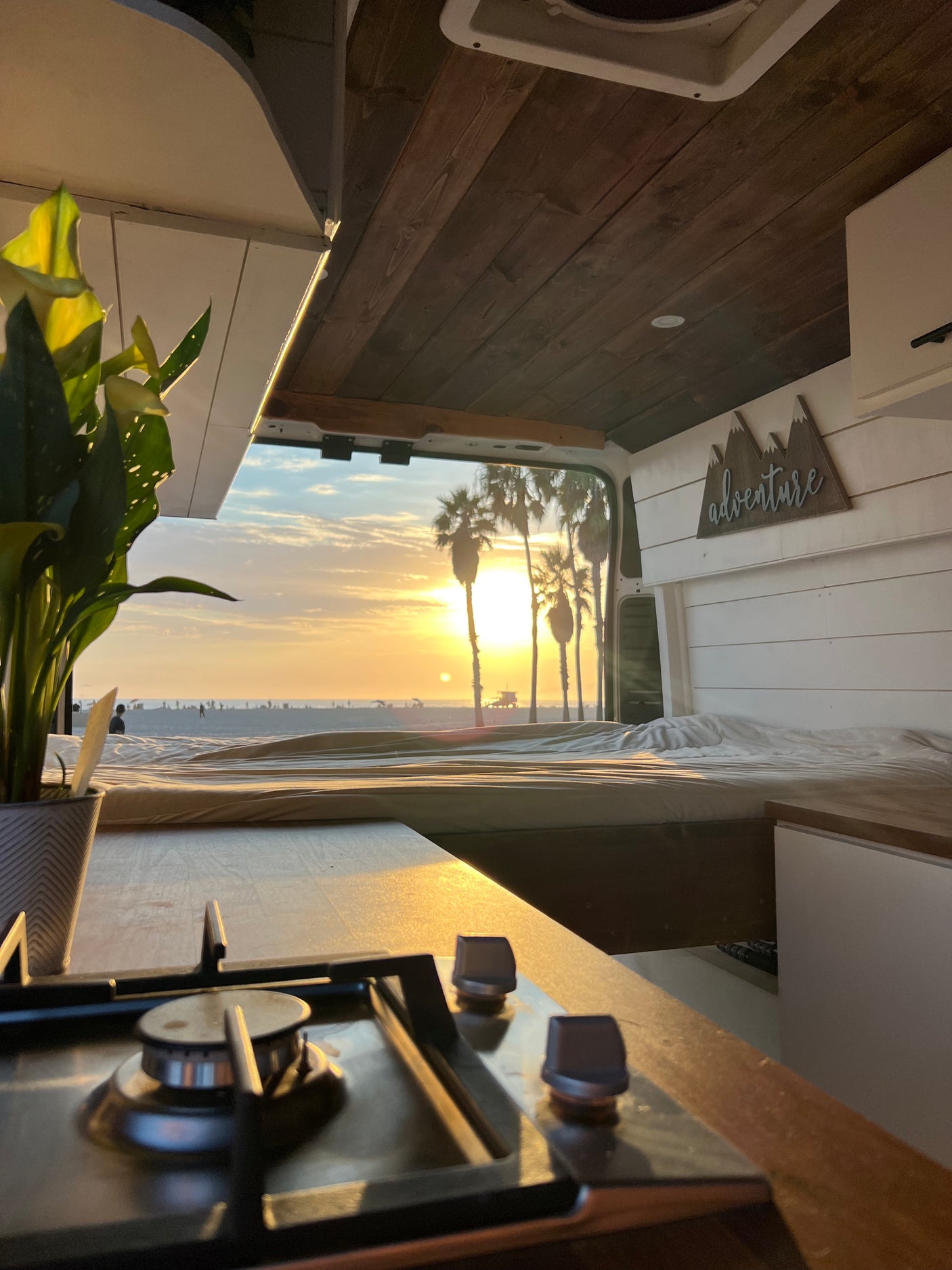 Cozy RV rental with stunning sunset beach views. Features a bed, kitchen, and 'adventure' sign for your travels.