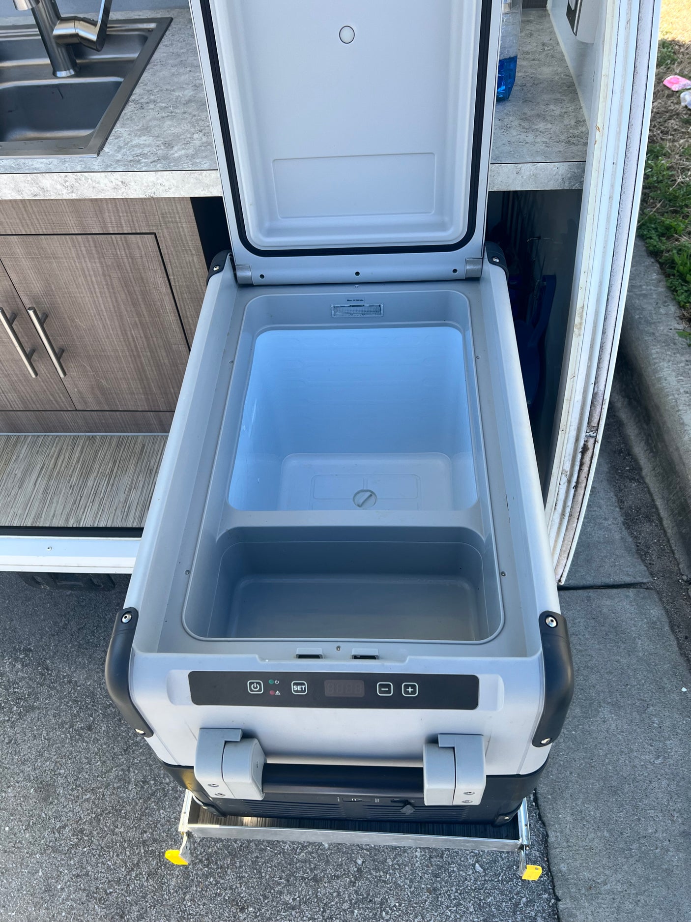 An open portable cooler/refrigerator on a slide-out tray, part of an RV rental kitchen setup with a sink.