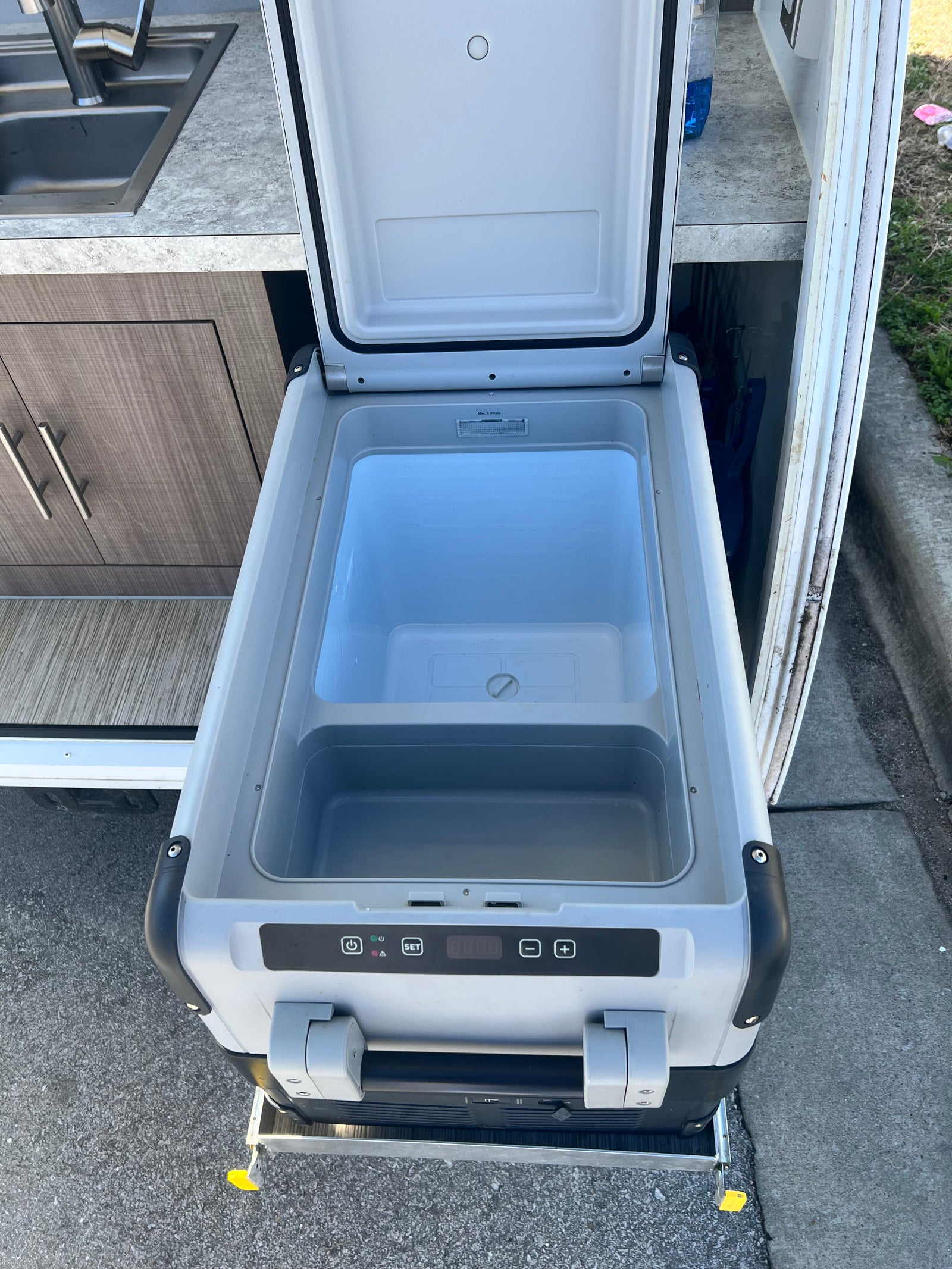 An open portable cooler/refrigerator on a slide-out tray, part of an RV rental kitchen setup with a sink.