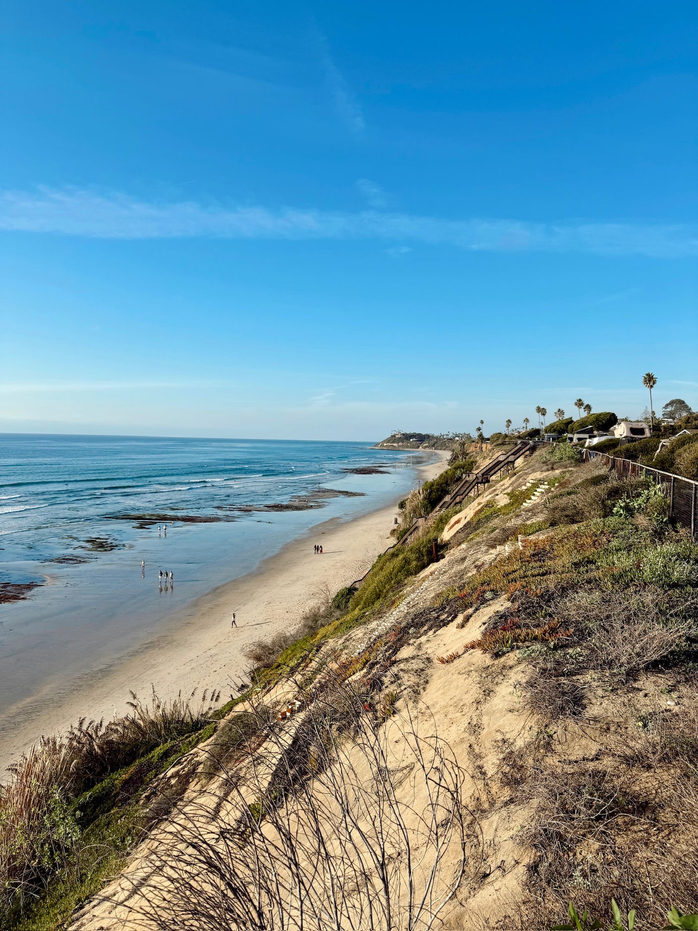 Coastal beach view from bluffs, ocean and people below. An RV is parked by cliffside homes, perfect for an RV rental vacation.