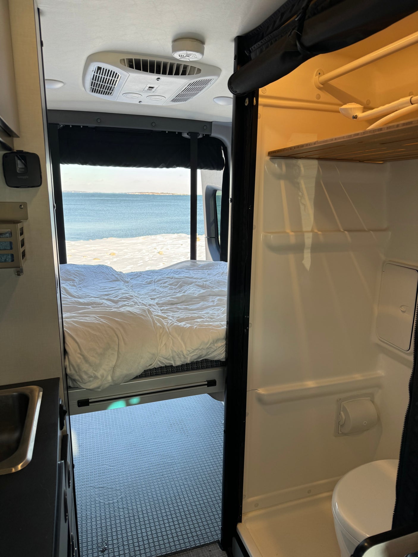 Cozy rv rental interior with a bed overlooking a snowy beach & ocean, featuring a sink area & compact bathroom.