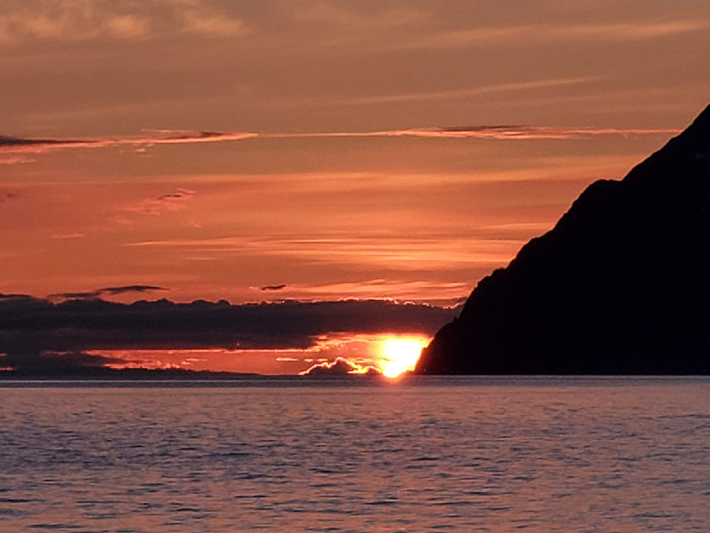 Vibrant sunset over calm waters, with the sun setting behind a dark mountain silhouette. Picture this view from your RV rental getaway.