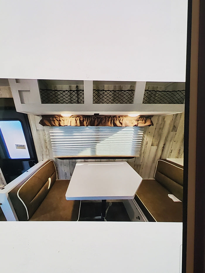 RV rental interior: cozy dinette with table, benches, window, and overhead storage, perfect for your next trip.