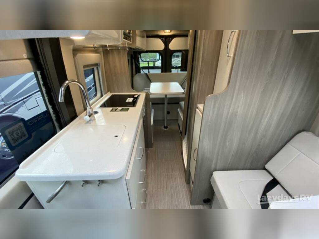 Well-equipped rv rental interior: view of compact kitchen with sink, stovetop, and dining area. Perfect for trips!